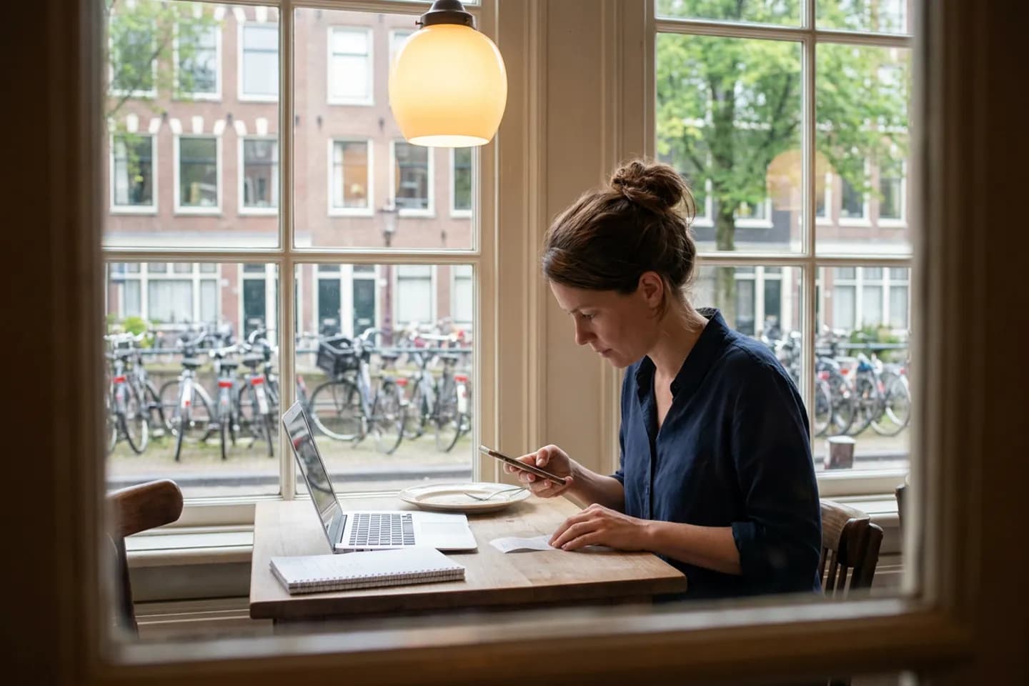 Een freelance journalist fotografeert een bonnetje met haar telefoon aan een cafétafel, naast haar laptop en notitieboek.